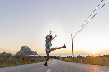 Young woman standing on street and lifting her leg at sunset, Ibiza - AFVF04374