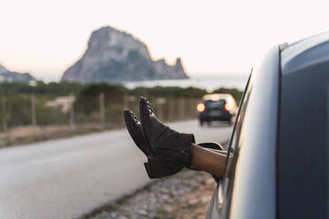 Junge Frau während einer Autofahrt, die Füße aus dem Fenster lehnend - AFVF04383