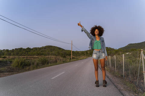 Junge Frau, die abends auf der Straße steht und trampen möchte, Ibiza, lizenzfreies Stockfoto