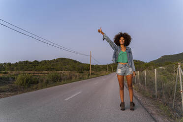 Young woman standing on street and hitchhiking in the evening, Ibiza - AFVF04396