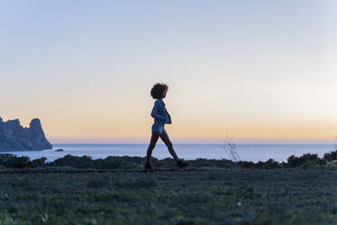 Junge Frau beim Spaziergang auf einer Wiese bei Sonnenuntergang, Ibiza - AFVF04400
