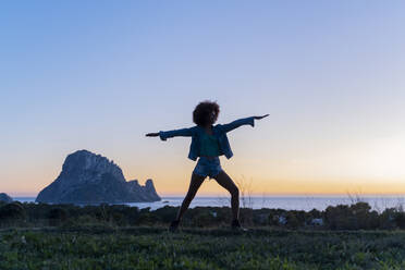 Junge Frau steht auf einer Wiese und macht Yoga bei Sonnenuntergang, Ibiza - AFVF04402
