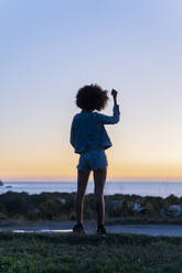 Rückansicht einer jungen Frau mit Hand in den Haaren, die auf einem Aussichtspunkt bei Sonnenuntergang steht, Ibiza - AFVF04403
