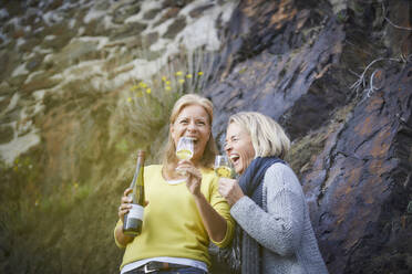 Zwei lachende reife Frauen trinken Wein im Freien - FMKF06044