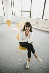 Smiling businesswoman sitting on a chair in an empty office - KNSF06869