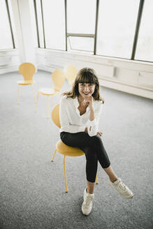 Lächelnde Geschäftsfrau sitzt auf einem Stuhl in einem leeren Büro - KNSF06869