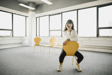 Smiling businesswoman sitting on a chair in an empty office - KNSF06872