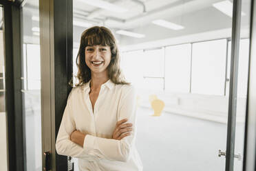 Smiling businesswoman standing in an open office door - KNSF06874