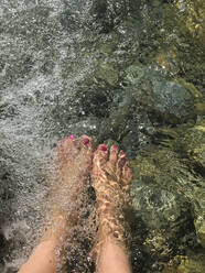 Woman refreshing feet in mountain river - GWF06328