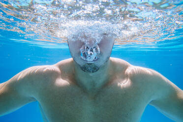 Unterwasseransicht eines Mannes im Schwimmbad, der Blasen aus dem Mund bläst - MIMFF00004