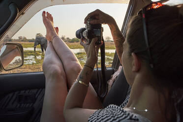 Woman taking a picture of an elephant out of the car window, Khwai, Botswana - VEGF01047