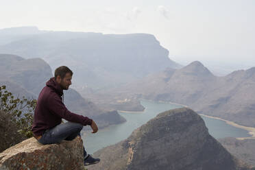Mann sitzt auf einem Felsen mit schöner Landschaft im Hintergrund, Blyde River Canyon, Südafrika - VEGF01064