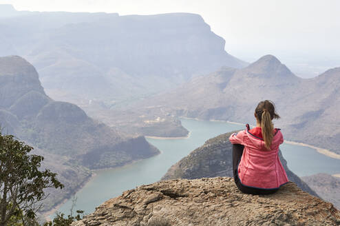 Frau sitzt auf einem Felsen und genießt die schöne Landschaft unter ihr, Blyde River Canyon, Südafrika. - VEGF01065