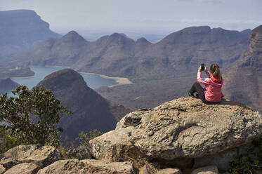 Frau, die ein Foto mit ihrem Handy vor dem Hintergrund einer wunderschönen Landschaft macht, Blyde River Canyon, Südafrika - VEGF01066