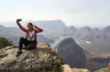 Woman taking a selfie with her cell phone with a beautiful landscape background, Blyde River Canyon, South Africa - VEGF01067