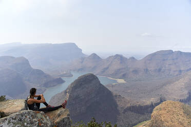 Frau sitzt auf einem Felsen mit schöner Landschaft im Hintergrund, Blyde River Canyon, Südafrika - VEGF01069