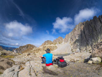 Älterer Mann, der eine Pause vom Wandern in einer Berglandschaft macht, Fleimser Alpen, Trentino, Italien - LAF02449