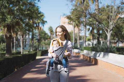 Mutter geht mit Baby im Tragetuch im Freien spazieren, lizenzfreies Stockfoto