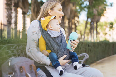 Glückliche Mutter ruht sich mit ihrem kleinen Jungen auf einer Parkbank aus - ERRF02237