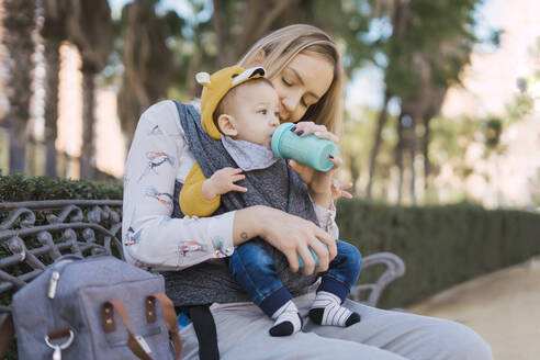 Mutter füttert kleinen Jungen auf einer Parkbank mit der Flasche - ERRF02238
