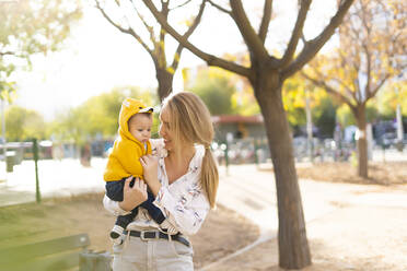 Happy mother carrying baby boy in a park - ERRF02264