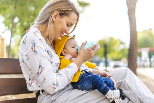 Mutter füttert kleinen Jungen auf einer Parkbank mit der Flasche - ERRF02275