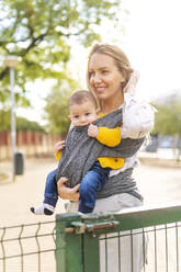 Happy mother carrying baby boy in a sling - ERRF02278