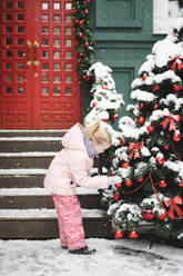 Kleines Mädchen betrachtet Weihnachtskugeln am Weihnachtsbaum im Freien - EYAF00738
