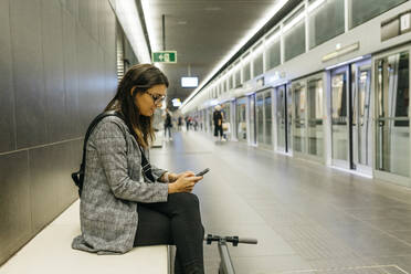 Junge Geschäftsfrau mit E-Scooter beim Telefonieren in der U-Bahn-Station - JRFF03893