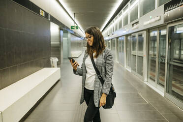 Junge Geschäftsfrau, die in der U-Bahn-Station telefoniert und auf den Zug wartet - JRFF03898