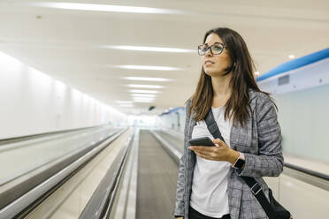 Young businesswoman using smartphone on moving walkway - JRFF03900