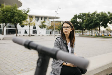 Young businesswoman with e-scooter in the city, looking sideways - JRFF03907