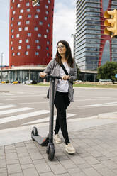 Young businesswoman walking with e-scooter in the city - JRFF03911