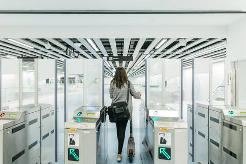 Junge Frau, die in der U-Bahn mit ihrem Elektroroller eine Kontrolle durchführt, lizenzfreies Stockfoto