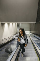 Geschäftsfrau auf Rolltreppe einer U-Bahn-Station stehend - JRFF03924