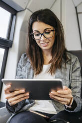 Brunette woman while traveling by train to work, with a tablet in her hands - JRFF03927