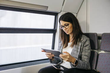 Brunette woman while traveling by train to work, with a tablet in her hands - JRFF03928