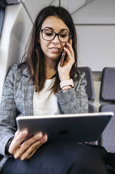 Brunette woman while traveling by train to work, using smartphone and a tablet - JRFF03929