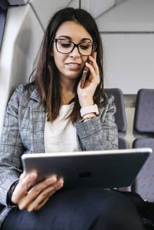 Brünette Frau, die mit dem Zug zur Arbeit fährt und ein Smartphone und ein Tablet benutzt - JRFF03929