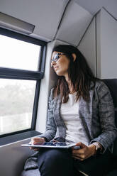 Brünette Frau auf dem Weg mit dem Zug zur Arbeit, mit einem Tablet in den Händen - JRFF03930