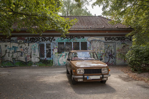 Deutschland, Berlin, Brauner Oldtimer geparkt vor einem mit Graffiti beschmierten Gebäude - JMF00472