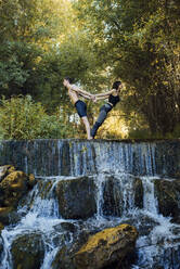 Paar übt gemeinsam Acro-Yoga an einem Wasserfall - MIMFF00007