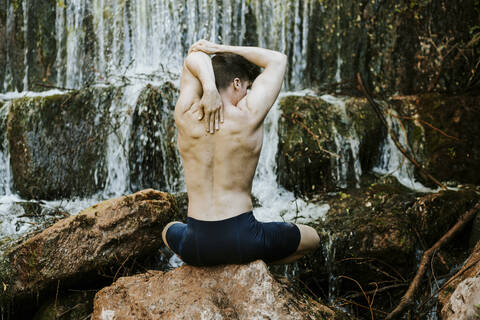 Rückansicht eines jungen Mannes, der an einem Wasserfall Yoga übt, lizenzfreies Stockfoto