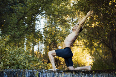 Junger Mann übt Yoga an einem Wasserfall, beugt sich über den Rücken - MIMFF00014