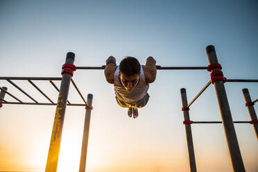 Junger Mann, der bei Sonnenaufgang in einer Turnhalle im Freien Gymnastik macht - MIMFF00022