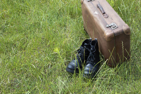 Alter brauner Lederkoffer und ein Paar schwarze Stiefel auf einer Wiese - PSTF00487