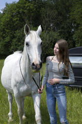 Happy teenage girl standing on a meadow with horse - PSTF00506