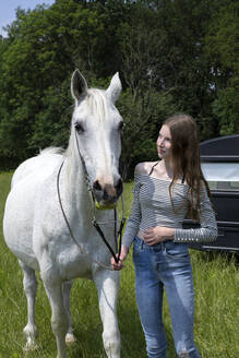 Glückliches Teenager-Mädchen auf einer Wiese stehend mit Pferd - PSTF00506