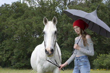 Porträt eines Mädchens auf einer Wiese mit Pferd und Regenschirm - PSTF00508