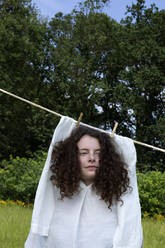 Porträt einer jungen Frau mit braunen Locken im weißen Kleid, die auf einer Wäscheleine trocknet - PSTF00532